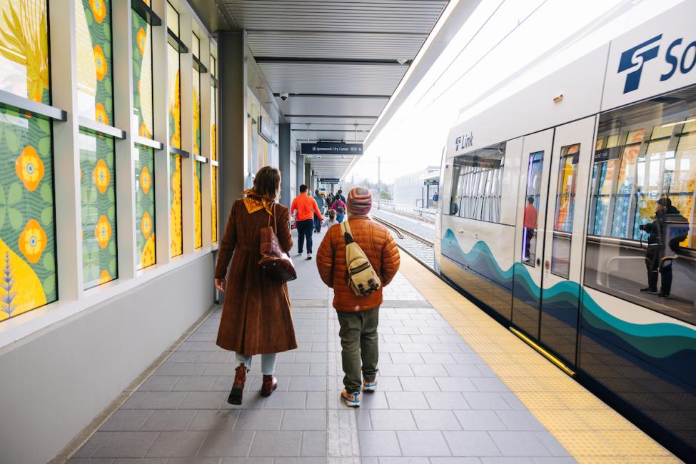 Two people with backpacks walk along the platform at Star Lake Station