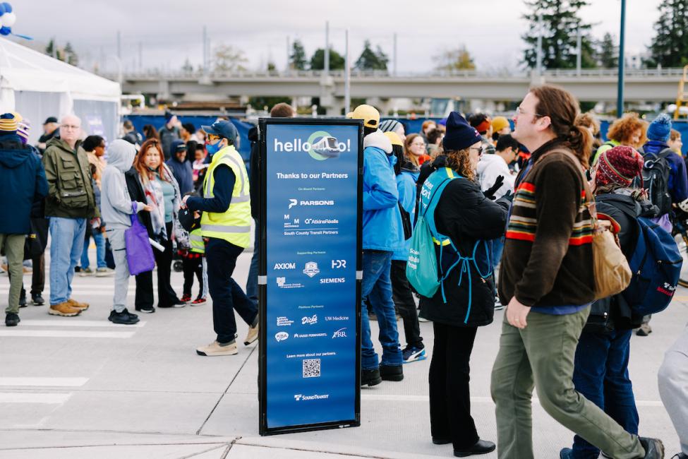 People walk by a Sound Transit sign recognizing sponsors