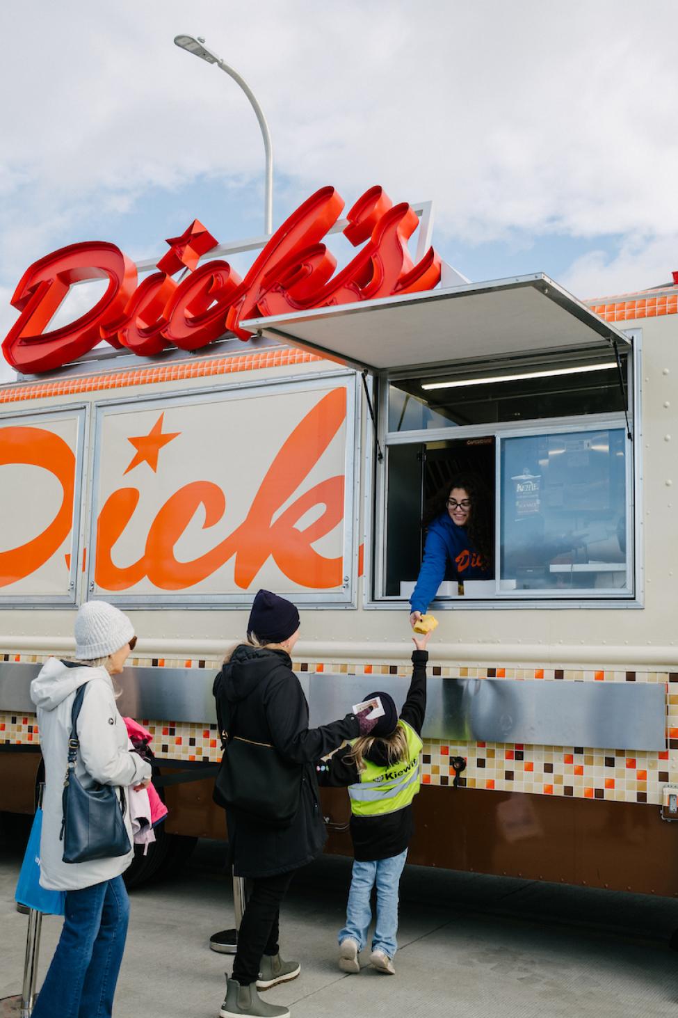 A Dick's employee hands a burger out to a child through their food truck window