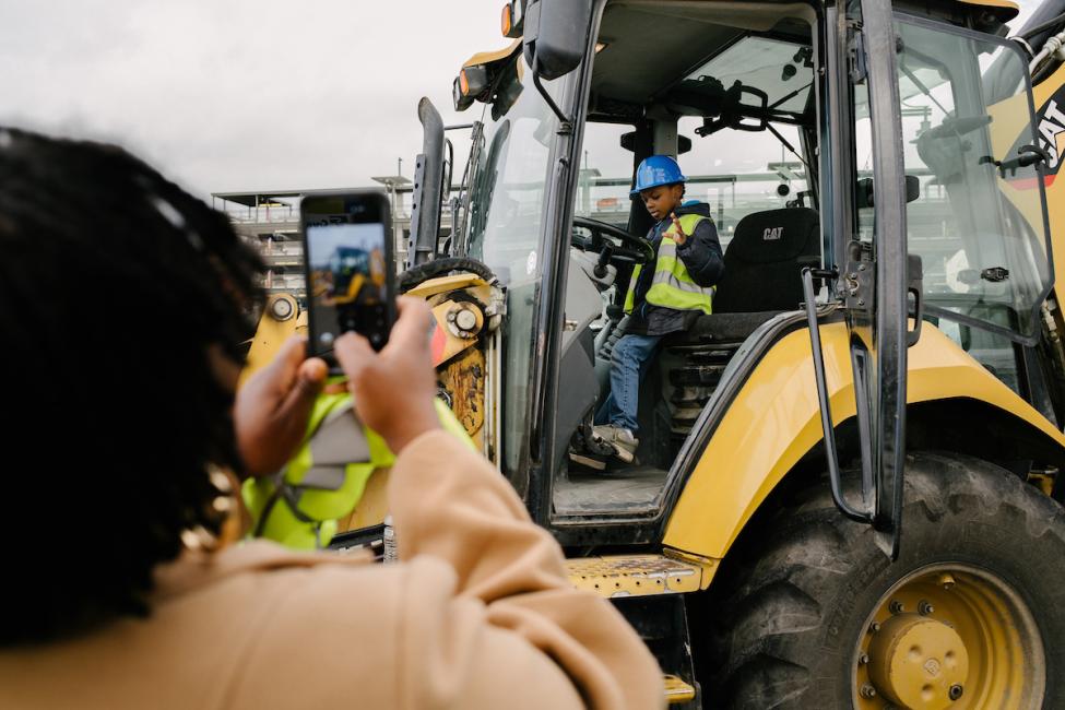 A child sits on a piece of construction equipment and smiles