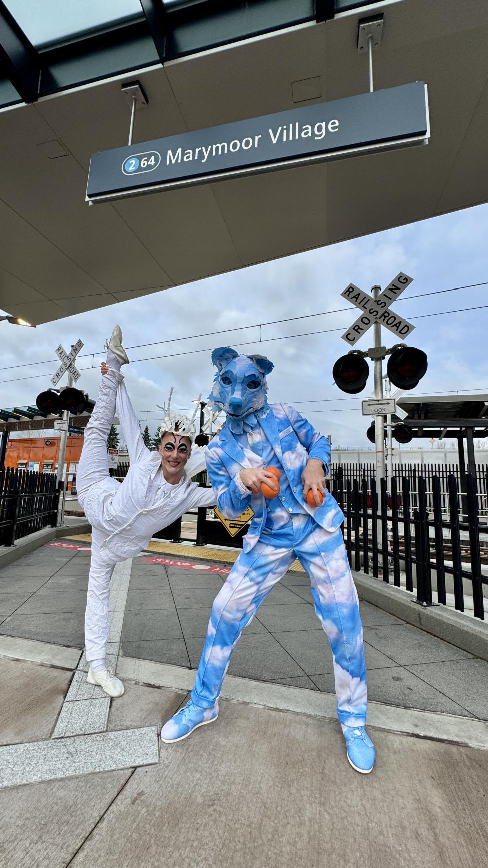 Two cirque performers stand in front of Marymoor Village Station signage