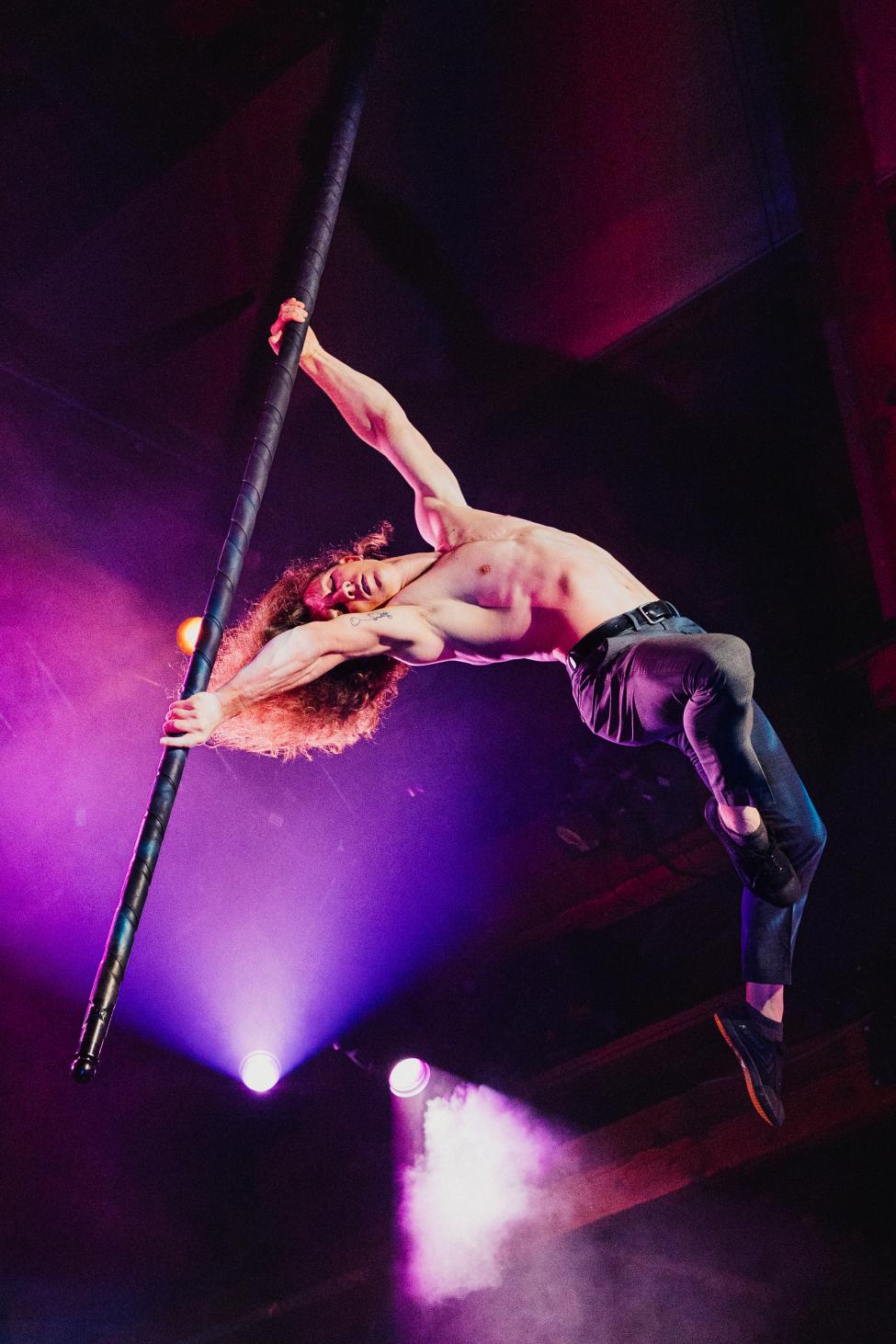A performer performs acrobatics on a pole while shirtless 