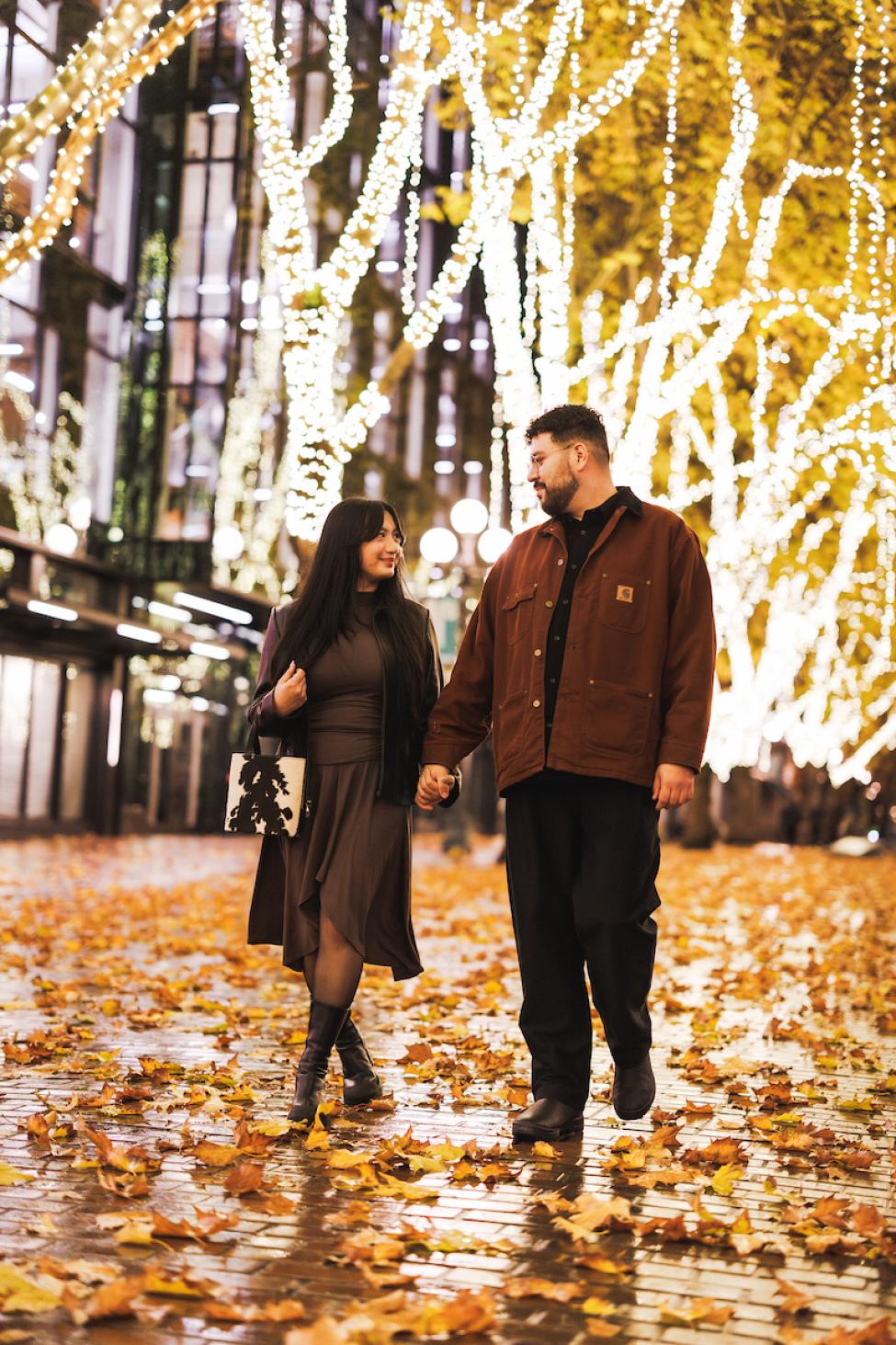 Two people walk through Occidental Park amongst twinkling lights in the trees. 