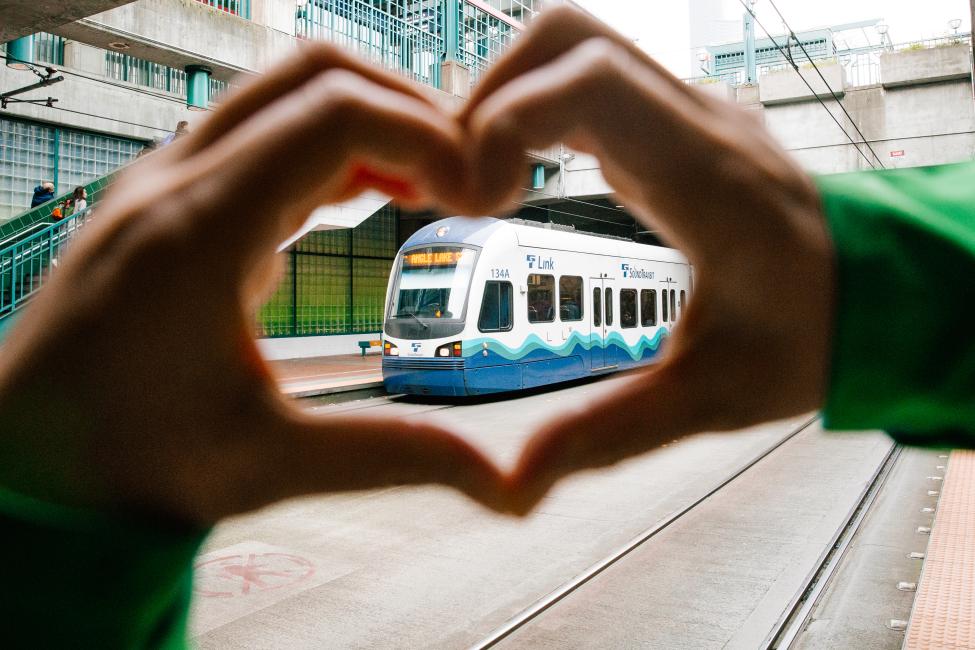 A person makes 'heart hands' around a Link train at International District/Chinatown Station,