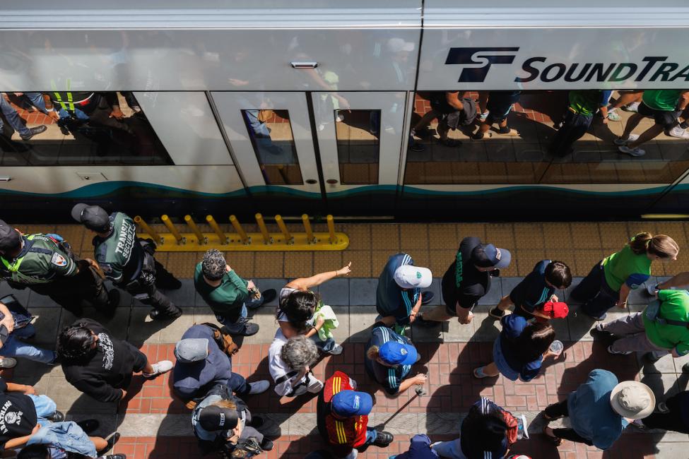 Soccer fans walk along a Link platform next to a train. The angle of the photo is shot from directly above