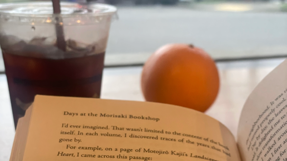A book, an iced coffee, and an orange on a table