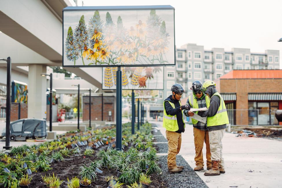 Three people in protective gear stand near art panels at Downtown Redmond Station