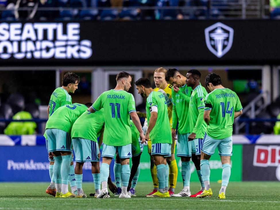 Seattle Sounders players huddle at midfield during a night game