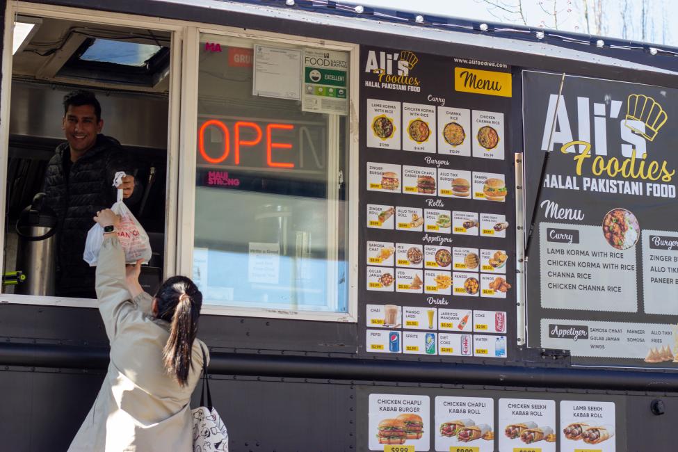 A person in a ponytail picks up a meal from a food truck