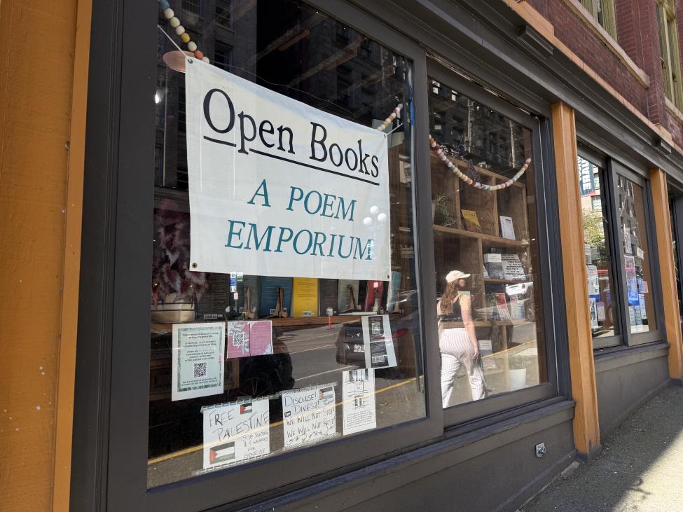 A large white sign in a storefront window reads "Open Books A Poem Emporium" in black and blue lettering