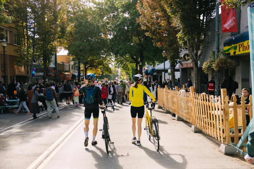 Two people walk their bicycles through a street festival in the U District neighborhood