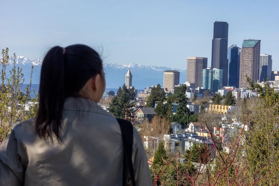 A person with dark hair in a ponytail looks out over the Seattle skyline on a sunny day
