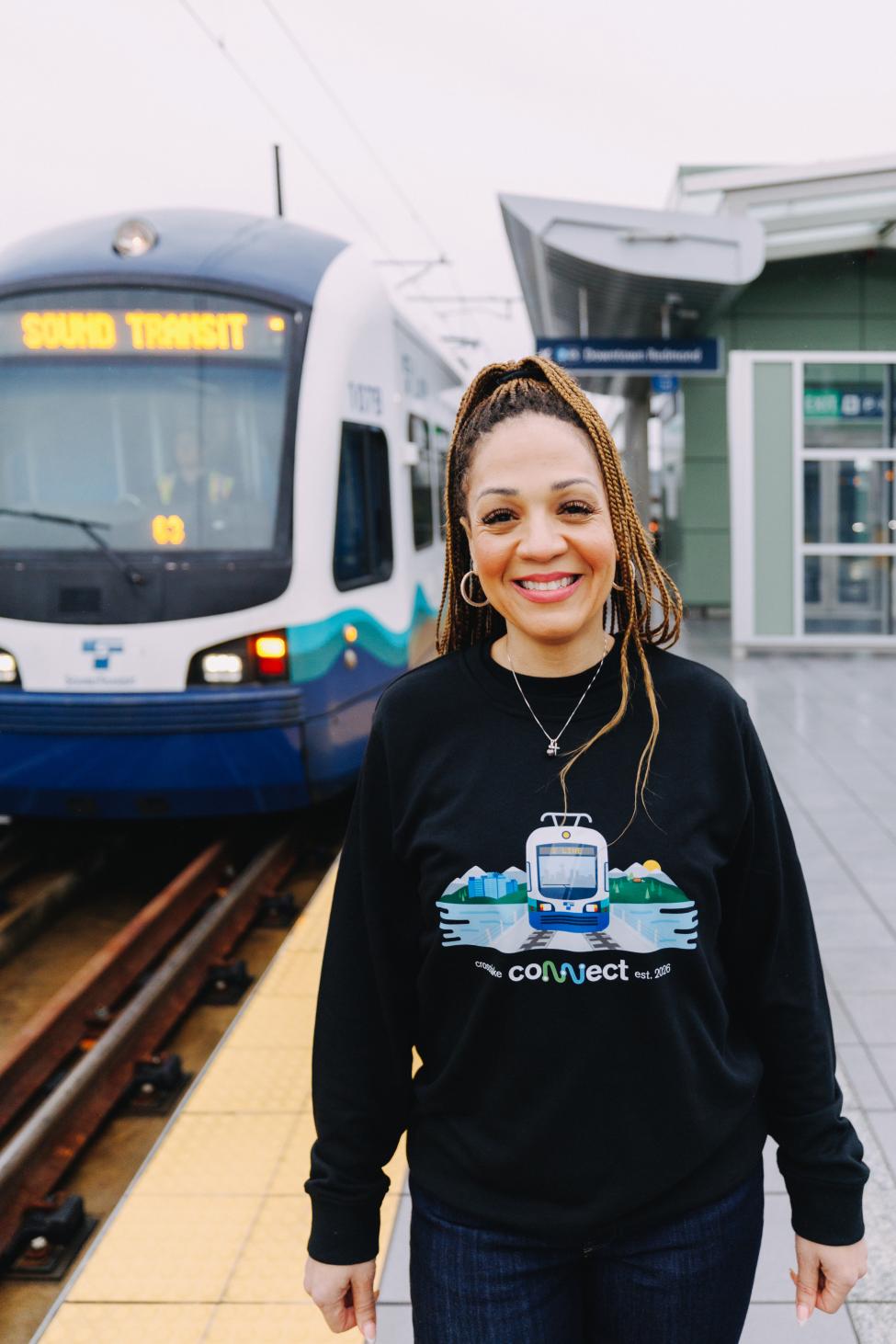 A person stands in front of a parked train with a Crosslake sweater on