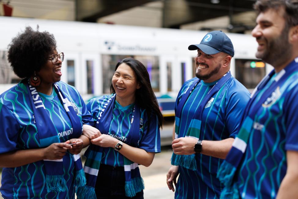 Four people in blue jerseys stand on the train platform at International District/Chinatown Station
