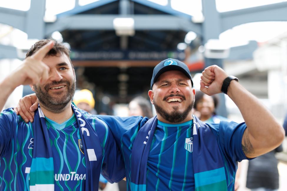 Two people wearing blue jerseys cheer while walking away from Stadium Station