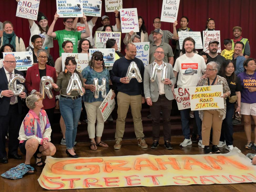 A group of about 30 people hold balloons and signs supporting Graham Street and Boeing Access Road stations