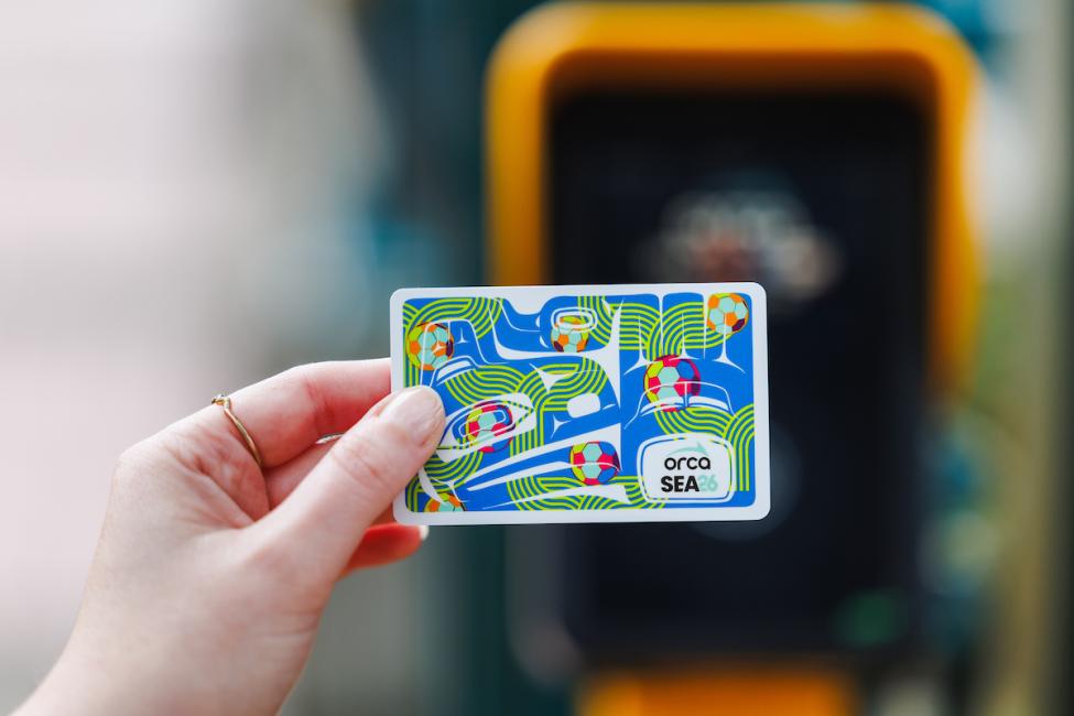 A hand holding a World Cup ORCA card in front of a yellow tapper