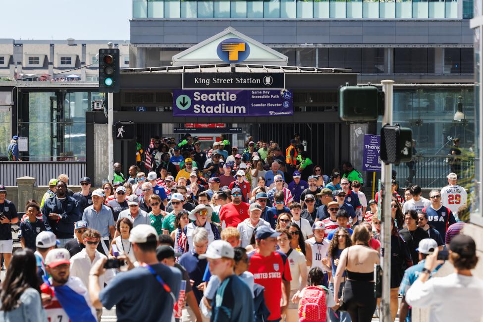 Crowds of people walk toward Weller Street Bridge and Seattle Stadium on a sunny summer day
