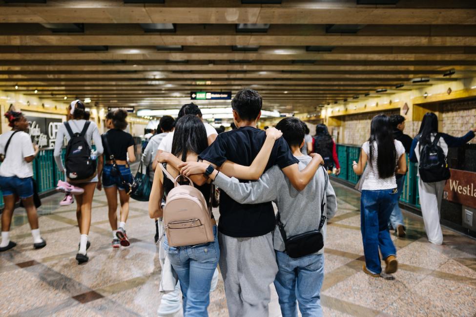 Three young people walk through Westlake Station wearing backpacks 