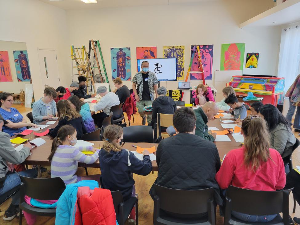 A classroom-type environment with people sitting at desks and art on the walls