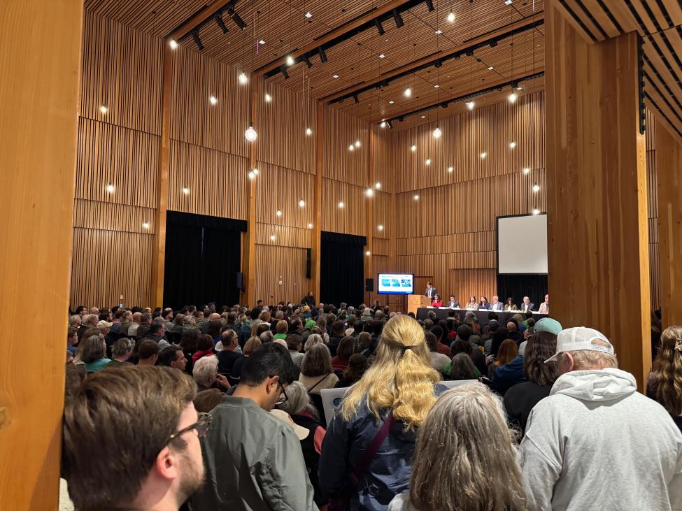A large crowd of people in a room with high ceilings and decorative wood walls