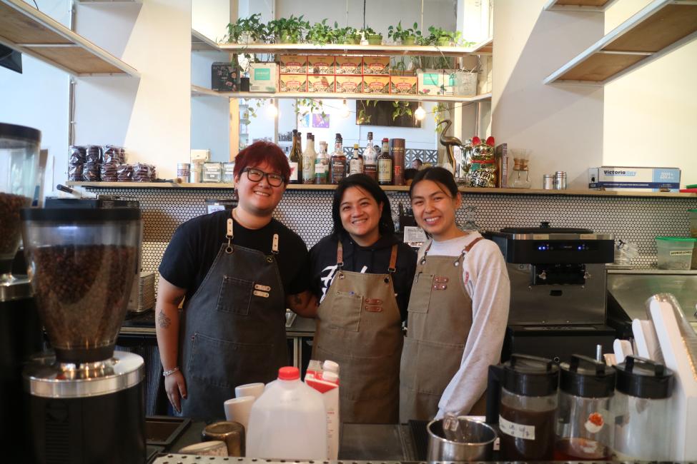Three people smile behind the bar of a coffee shop