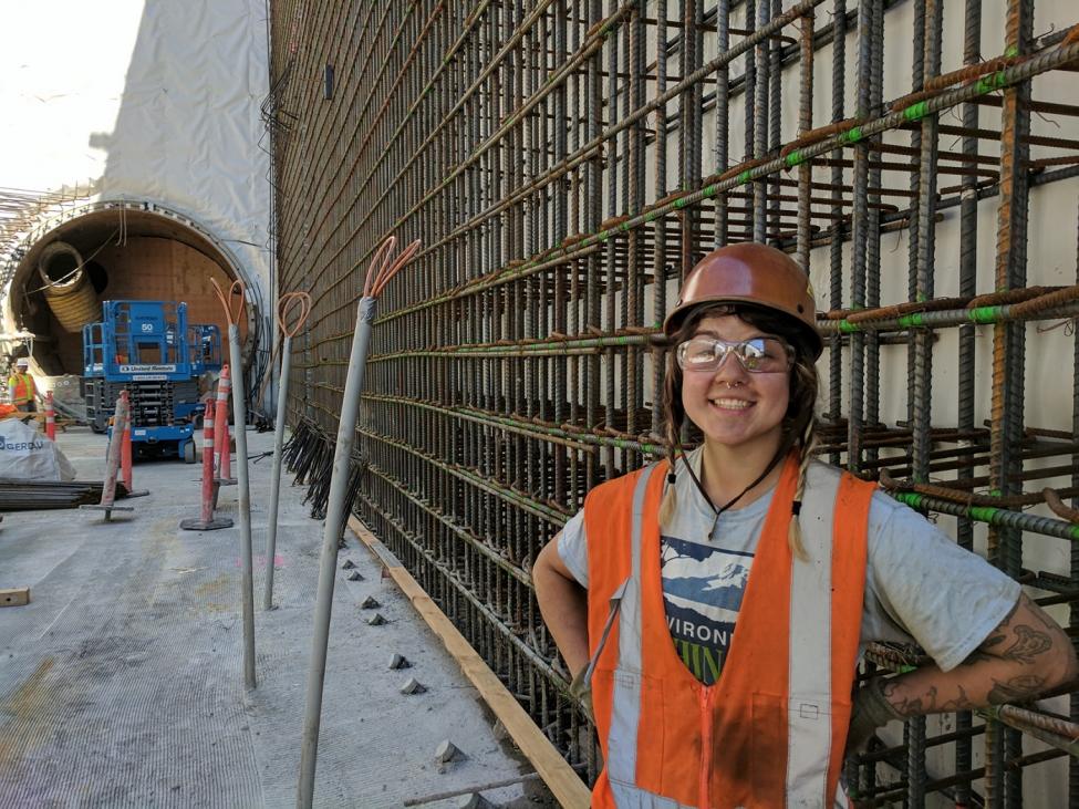 A young construction worker smiles in front of the steel rebar wall she will spend her day connecting with wire.