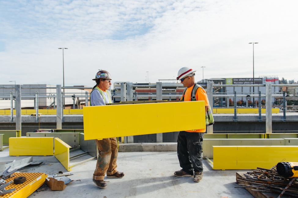 Workers carrying yellow panels on the platform of the future Northgate Link light rail station