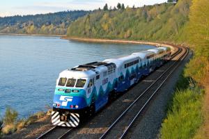 Sounder Everett train moving on tracks surrounded by trees and a lake.