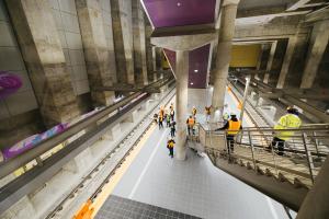 Looking down at the platform of the nearly complete Roosevelt Station, as media members descend the stairs.
