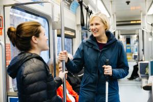 Jodi Mitchell holds a white cane and chats with a fellow passenger while standing on a Link train.