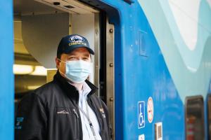 A Sounder conductor wears a blue face mask while standing in the doorway of the train.