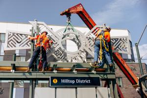 Workers install sculptures on top of the new Hilltop District station.