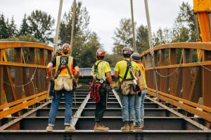 Four workers stand on the bridge, with their backs to the camera. 