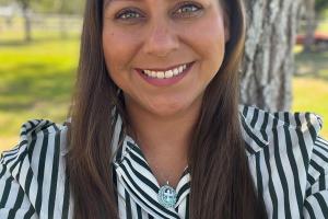 Valerie Valero smiles while wearing a striped shirt, with trees in the background. 