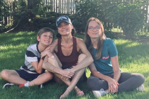 Clara O'Brien and her kids smile while sitting cross-legged on a grass lawn.