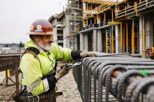 A worker in a red hard hat and yellow vest works with rebar.