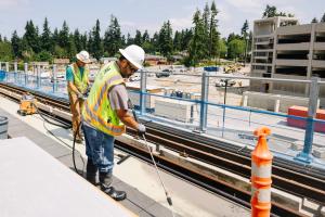 Crews in protective gear work on light rail tracks on a sunny day in Shoreline