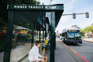 A passenger sits in a Pierce Transit bus shelter with a 590 bus approaching