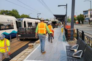 Crews in orange shirts and protective gear work on a Link station platform