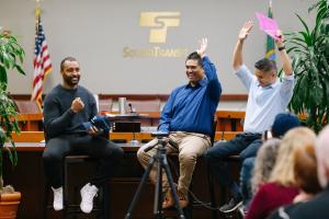 Doug Baldwin speaks to an audience in the Sound Transit board room with two ST employees 