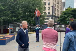 A person stands on the shoulder of our Sound Transit 'conductor' character while being filmed by a crew.