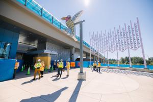 People in protective gear and yellow jackets look up at the 'Hummingbird' art at the future Lynnwood light rail station.