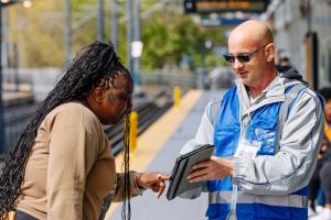 A surveyor wearing a blue vest talks to a Sound Transit passenger on a train platform