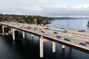 An aerial shot of the I-90 East Channel Bridge between Mercer Island and Bellevue. Cars and a Link light rail train cross the bridge on a sunny day.