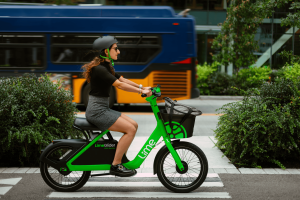 A woman rides a Lime Bike with a King County Metro bus going the opposite direction in the background.
