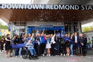A group of people celebrates the ceremonial ribbon cutting as confetti falls at Downtown Redmond Station.