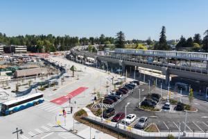 The light rail station in downtown Federal Way is nearing completion. Cars are parked at a lot by the elevated station, and an ST Express bus drives on a nearby road.