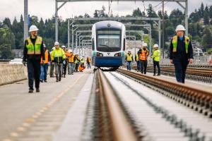 People in protective gear walk next to a Link light rail vehicle on the I-90 bridge during an unpowered tow test.