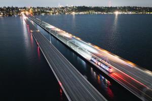 An aerial shot of a one-car Link light rail train crossing the I-90 floating bridge at nighttime.